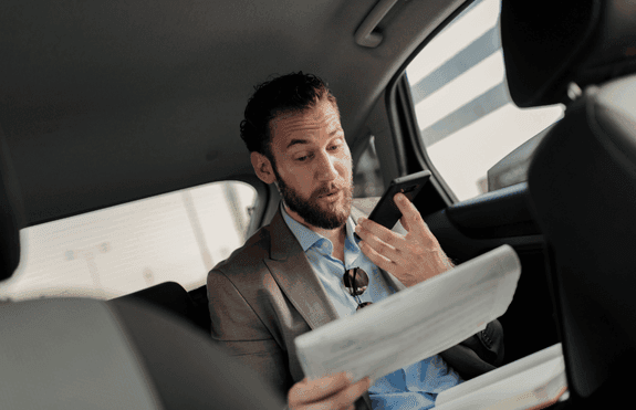 Ejecutivo leyendo documentos en el asiento trasero de un vehículo con chofer